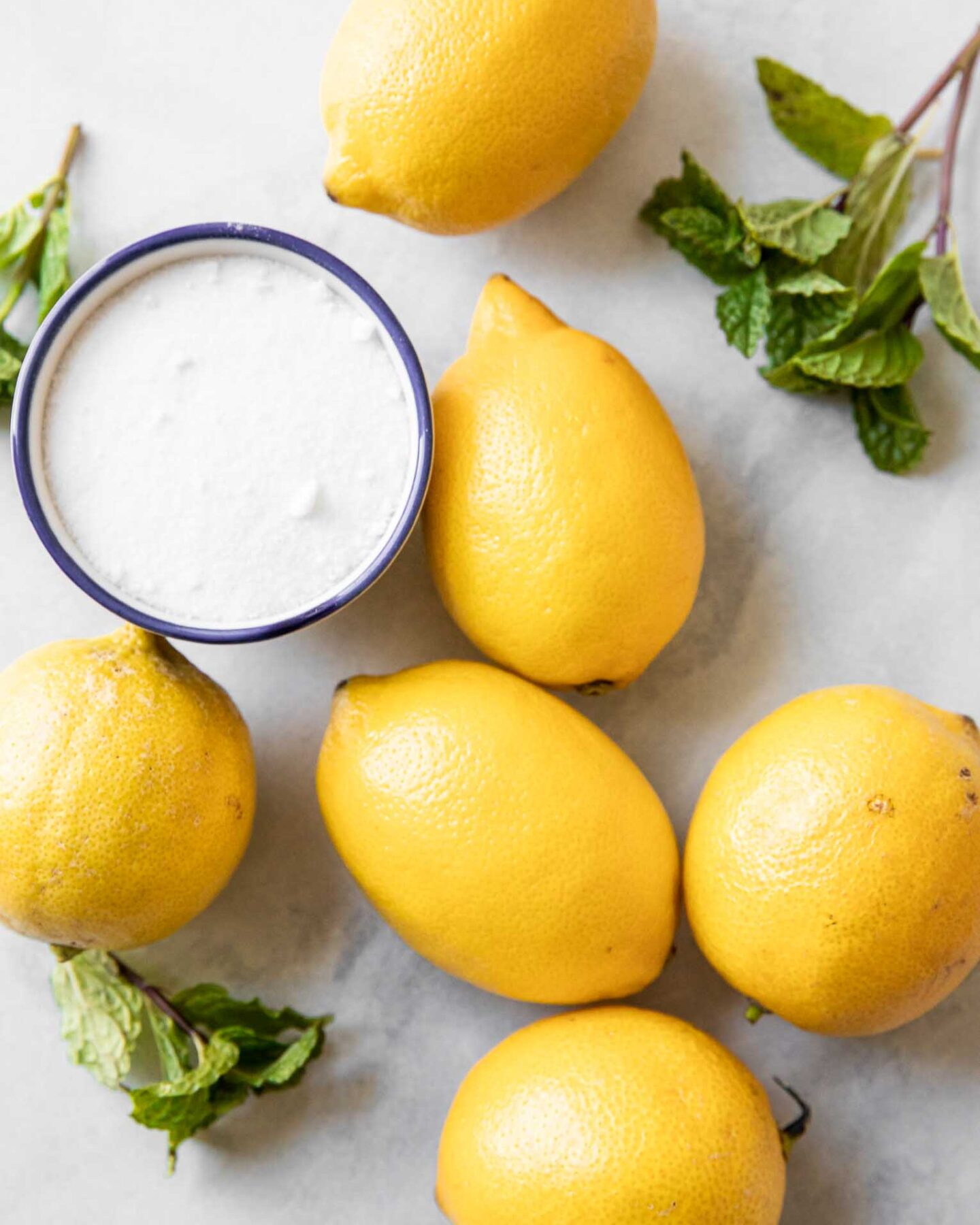 Lemons, sugar, and mint on a marble board.