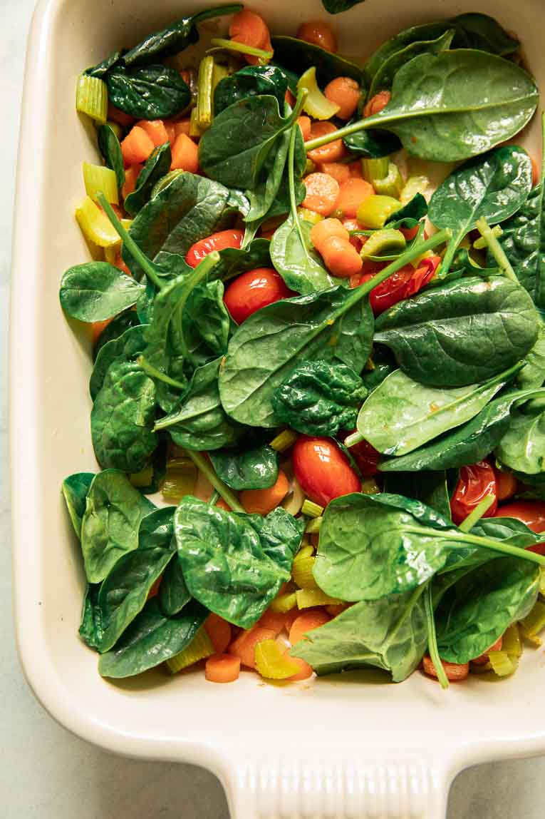 Roasted vegetables and fresh spinach in a baking dish.