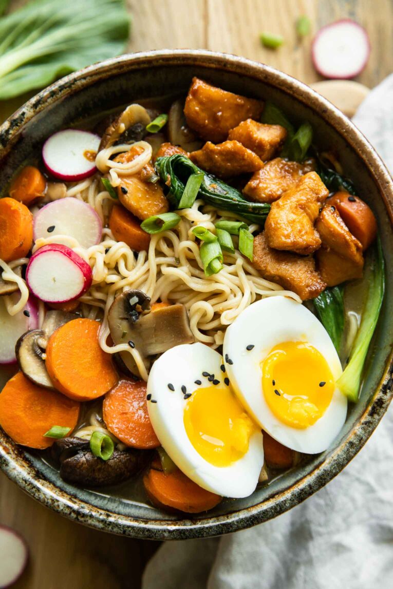 Close up of ramen, spicy chicken, radish, carrots, green onions, bok choy, and soft boiled eggs.
