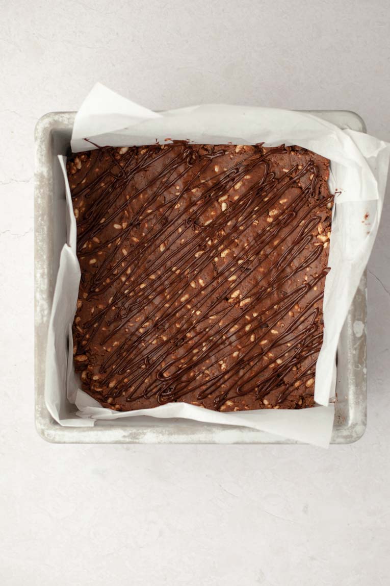 Chocolate drizzle over protein bar dough in a baking pan.
