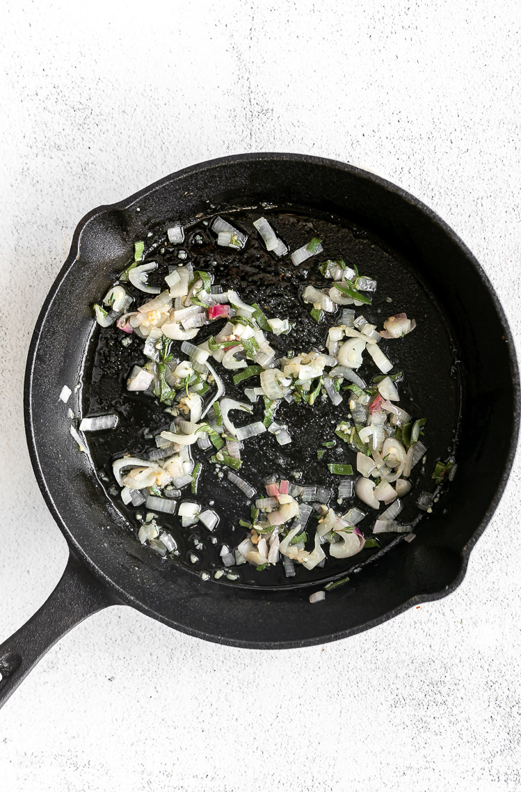 Shallot, garlic, and herbs being sautéed in a pan.
