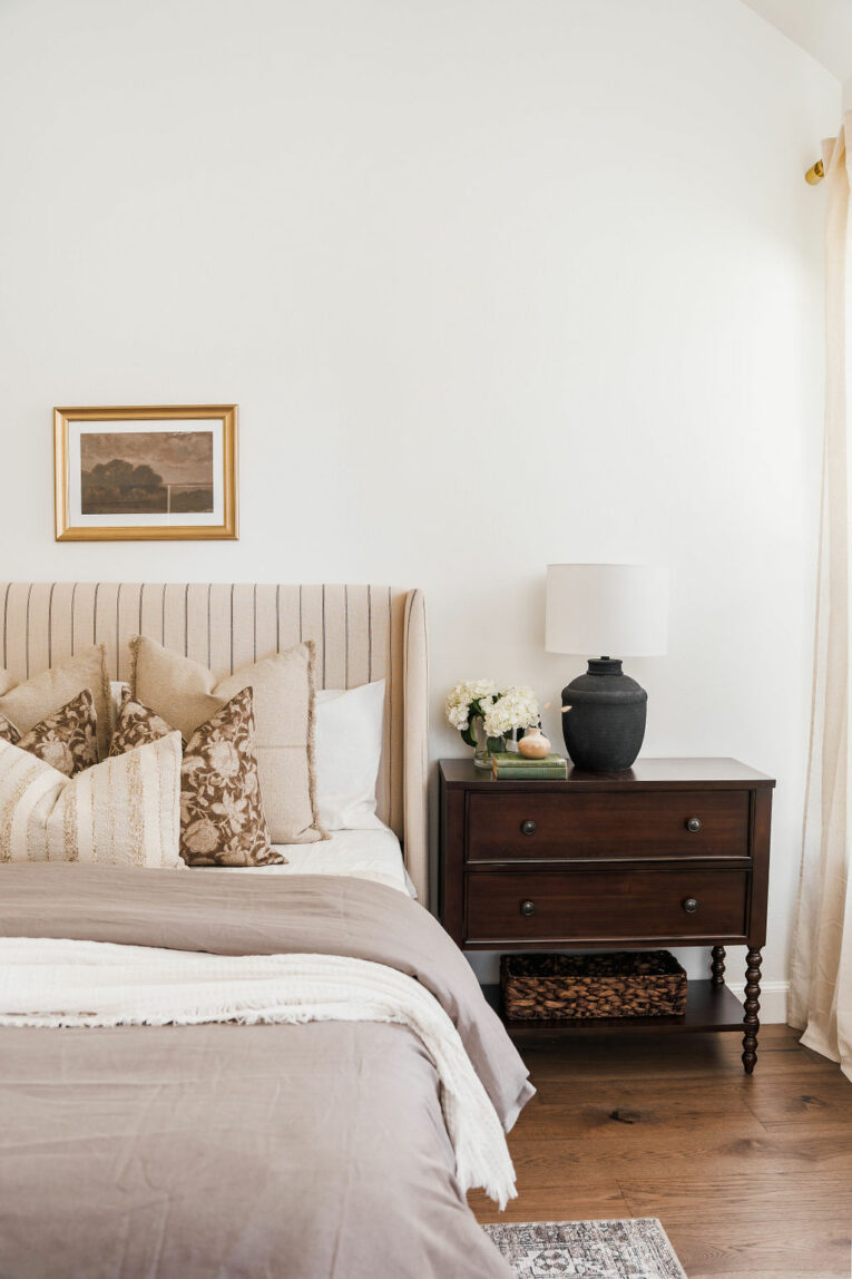 Bedroom with taupe bed and dark wood nightstand.