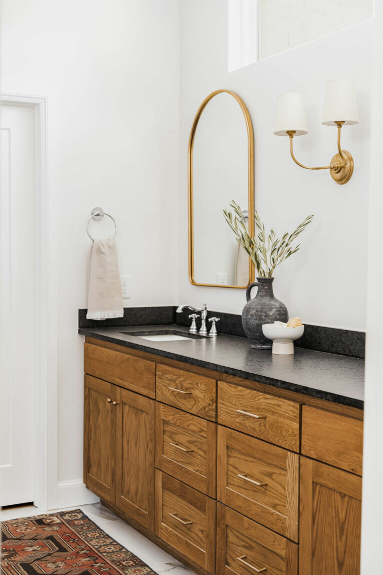 Arched gold mirrors and quartz countertops in bathroom.