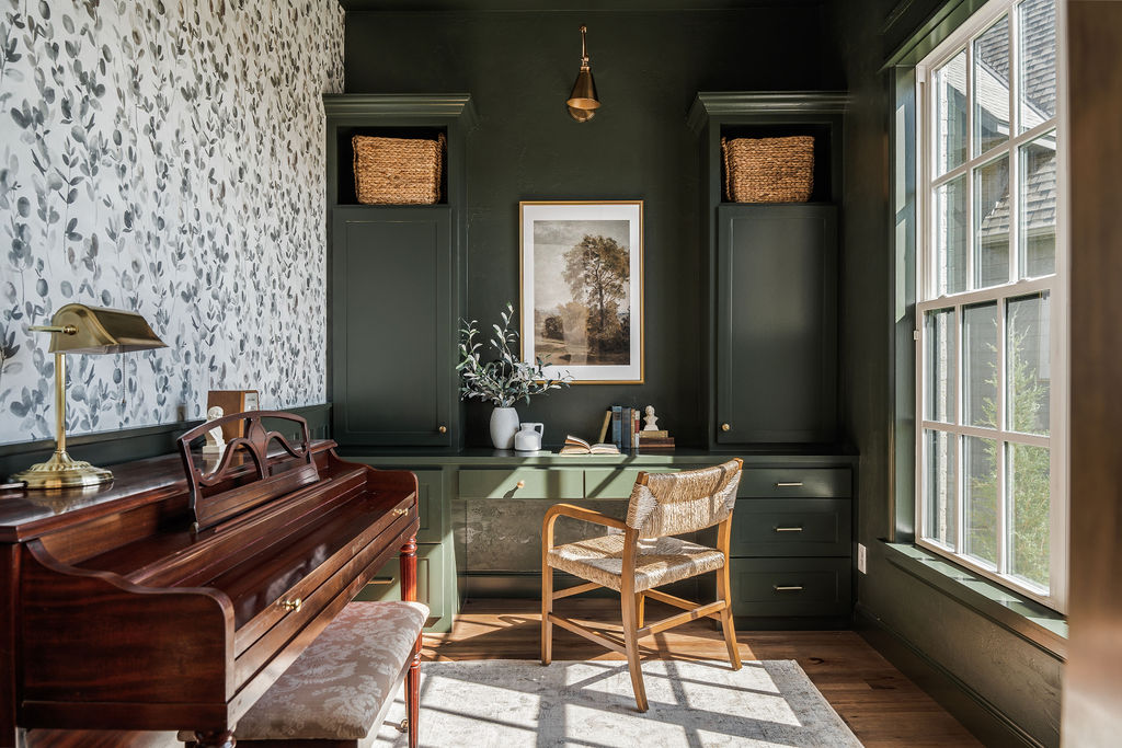 Dark green study with large window, floral wallpaper, gold fixtures and wood piano.