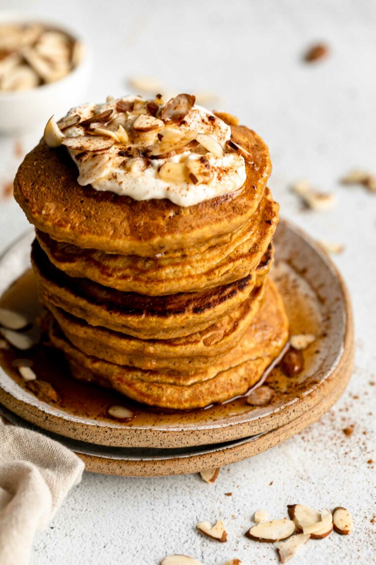 Angled photo of butternut squash pancakes with syrup, yogurt, and nuts on top.
