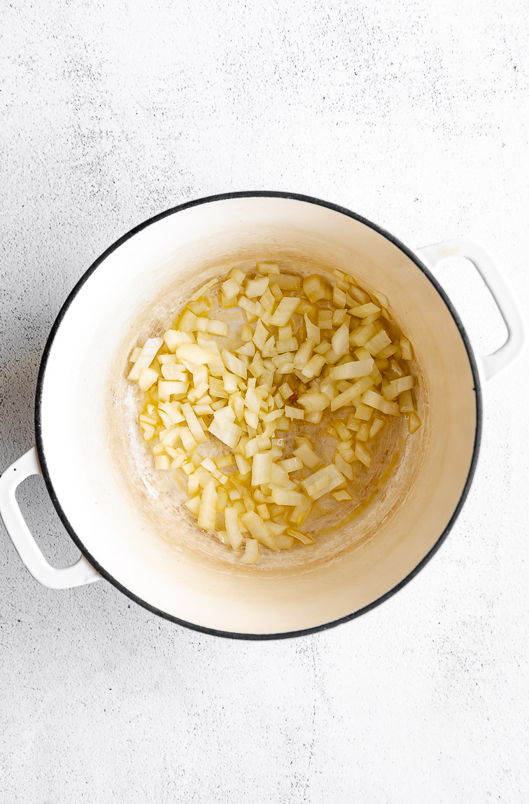 Olive oil and onions being cooked in a dutch oven.