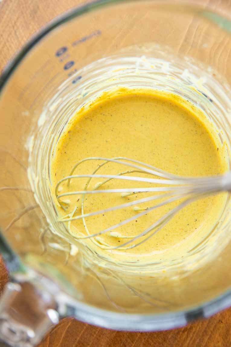 Creamy turmeric tahini sauce being whisked in a bowl.