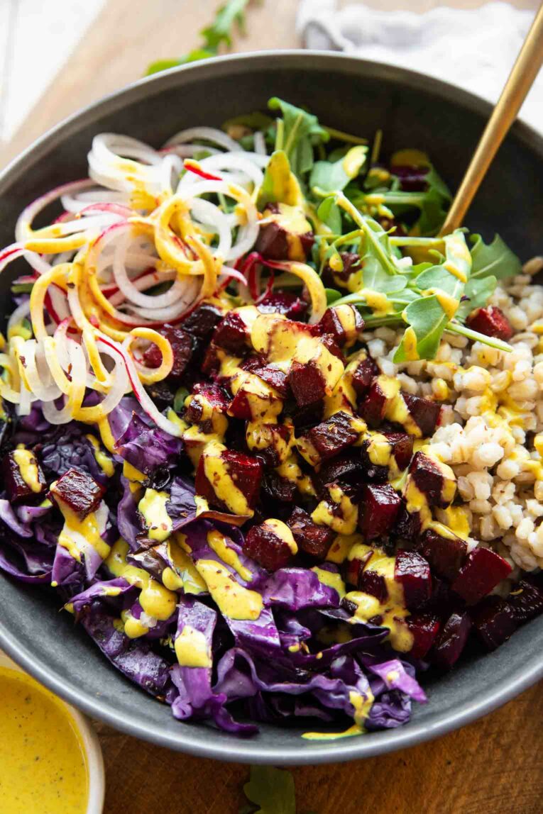 Angled photo of roasted beets in a bowl with arugula, cabbage, and grains.