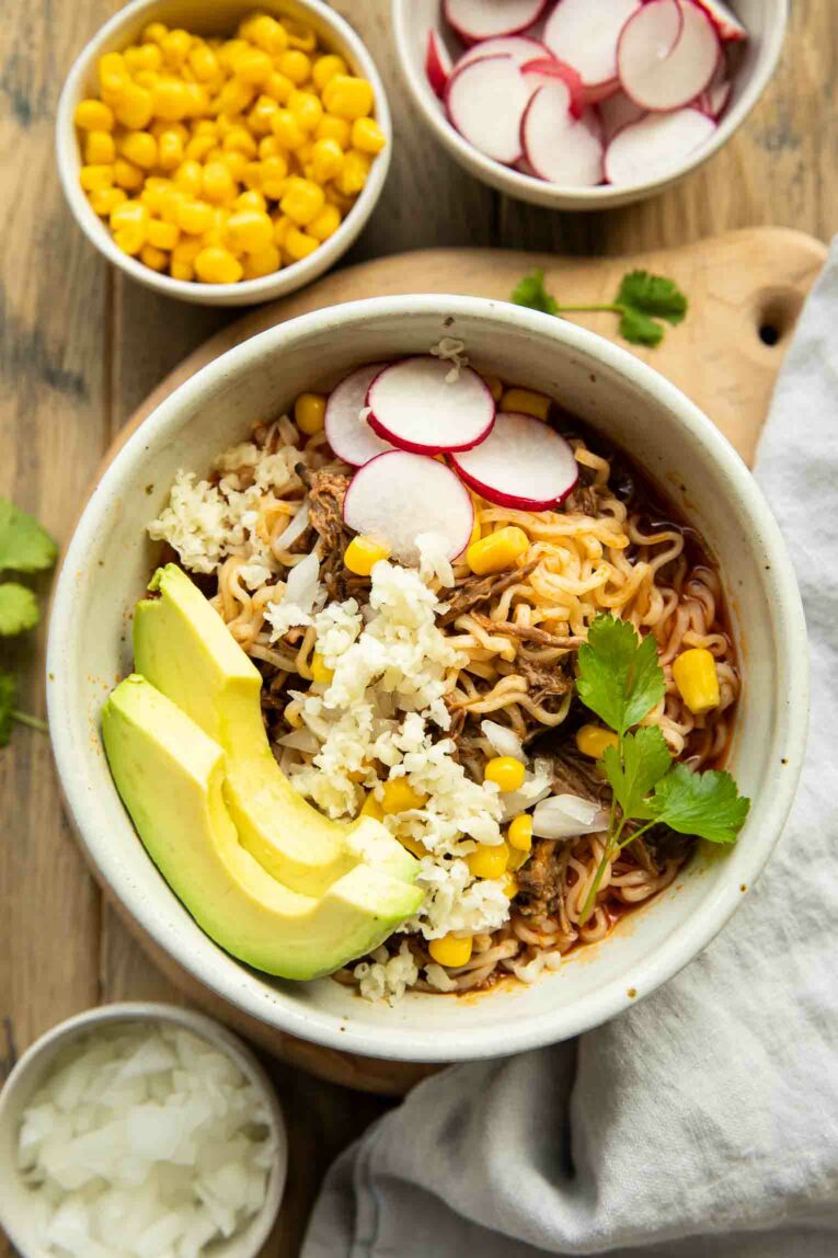 Birria ramen with radishes, cilantro, cheese, and avocado.