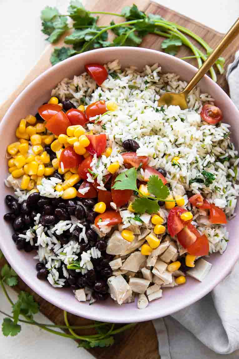 Cilantro Lime Rice, avocado, beans, chicken, tomatoes, and corn in a bowl.