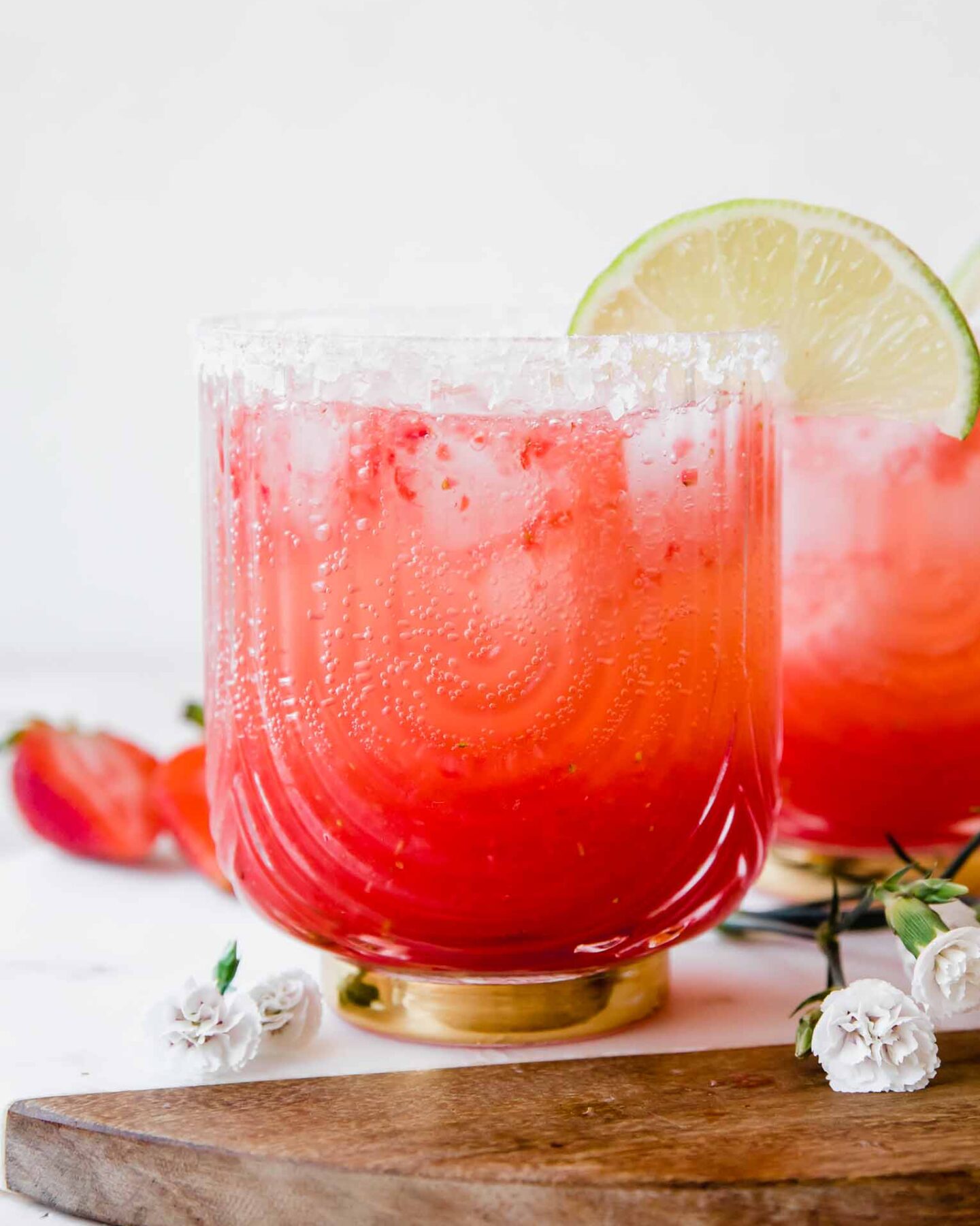 Strawberry Lime Mocktail Margarita recipe with lime, salt, and flowers in background.
