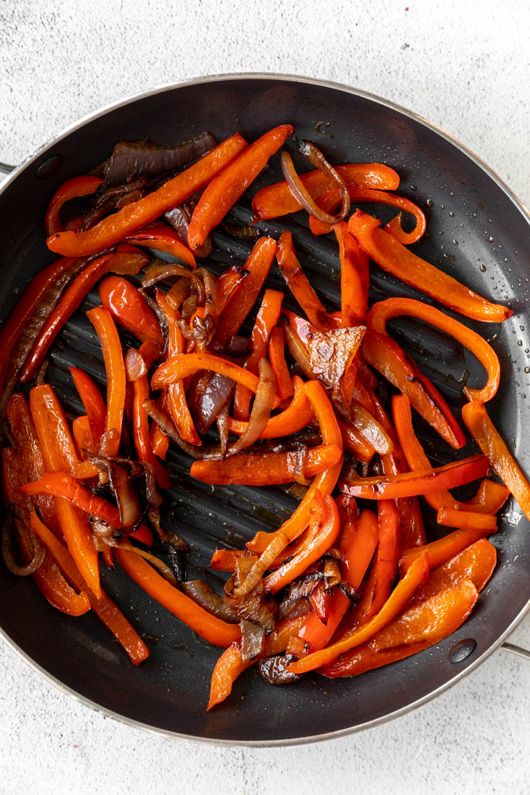 Red bell peppers and onions being sautéed.