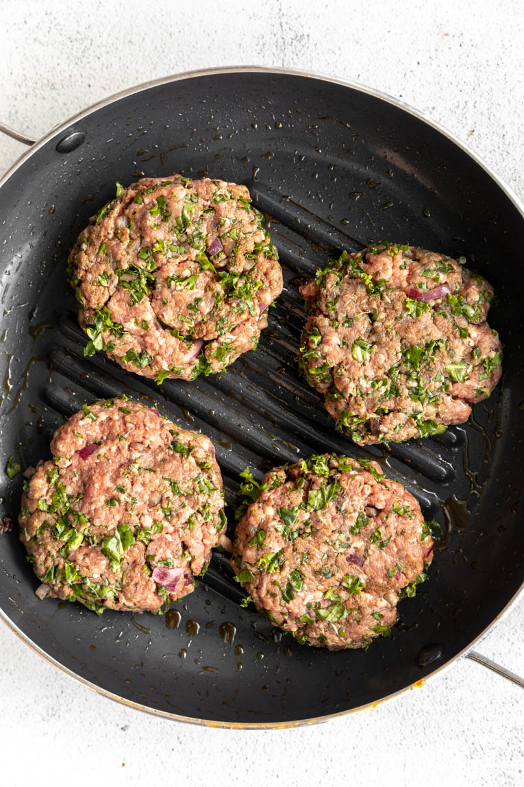 Kale beef burger patties in a cast iron skillet.