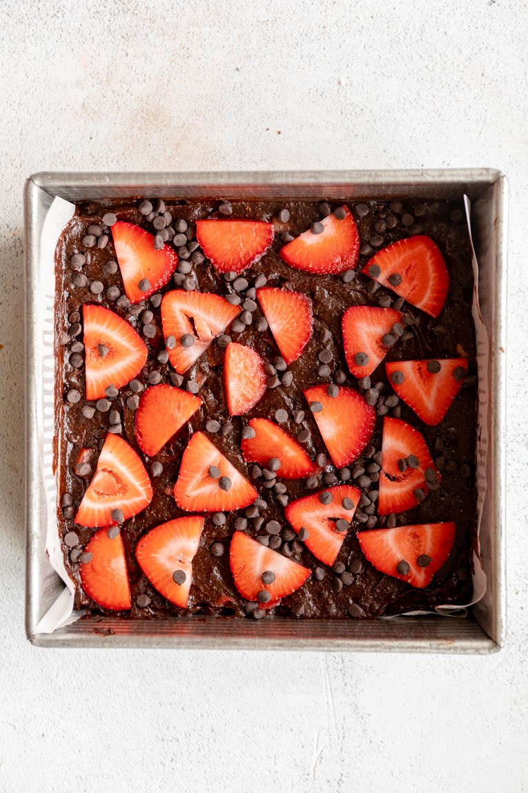 Chocolate strawberry brownie batter with sliced strawberries in a baking pan.
