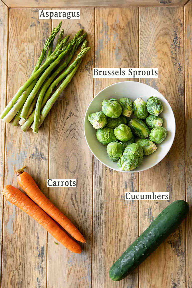 Asparagus, sprouts, carrots, and cucumber on a wood table.