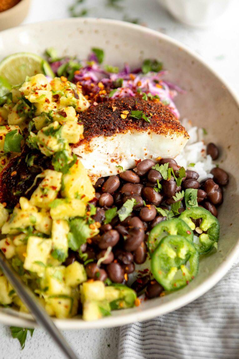 Angled photo of mahi mahi seasoned fish with pineapple salsa, jalapeƱos, beans, and rice.