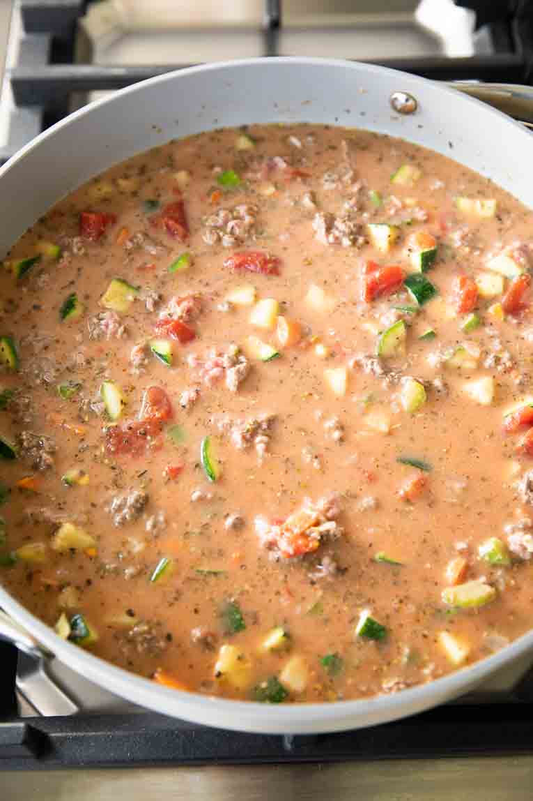 Milk and tomato sauce being mixed with veggies and beef.