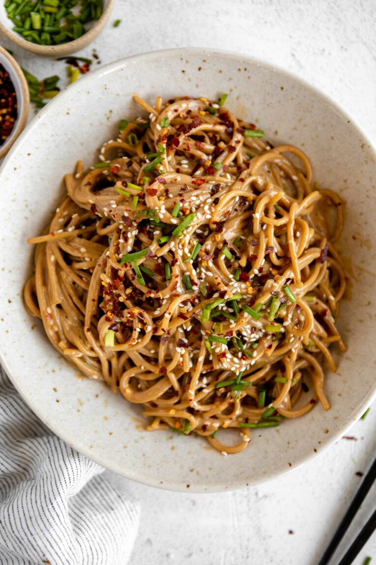 Sesame Tahini Noodles in a white bowl with chives, sesame seeds, and red pepper flakes.