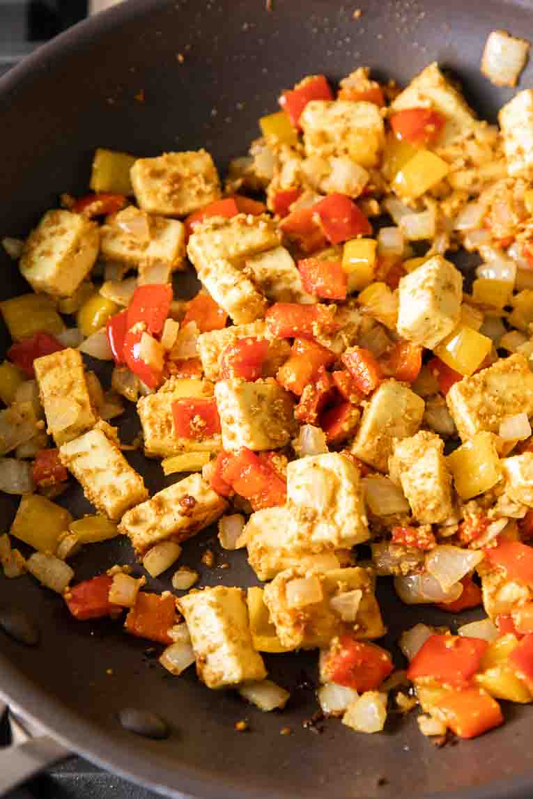 Paneer and vegetables being sautéed in a pan.