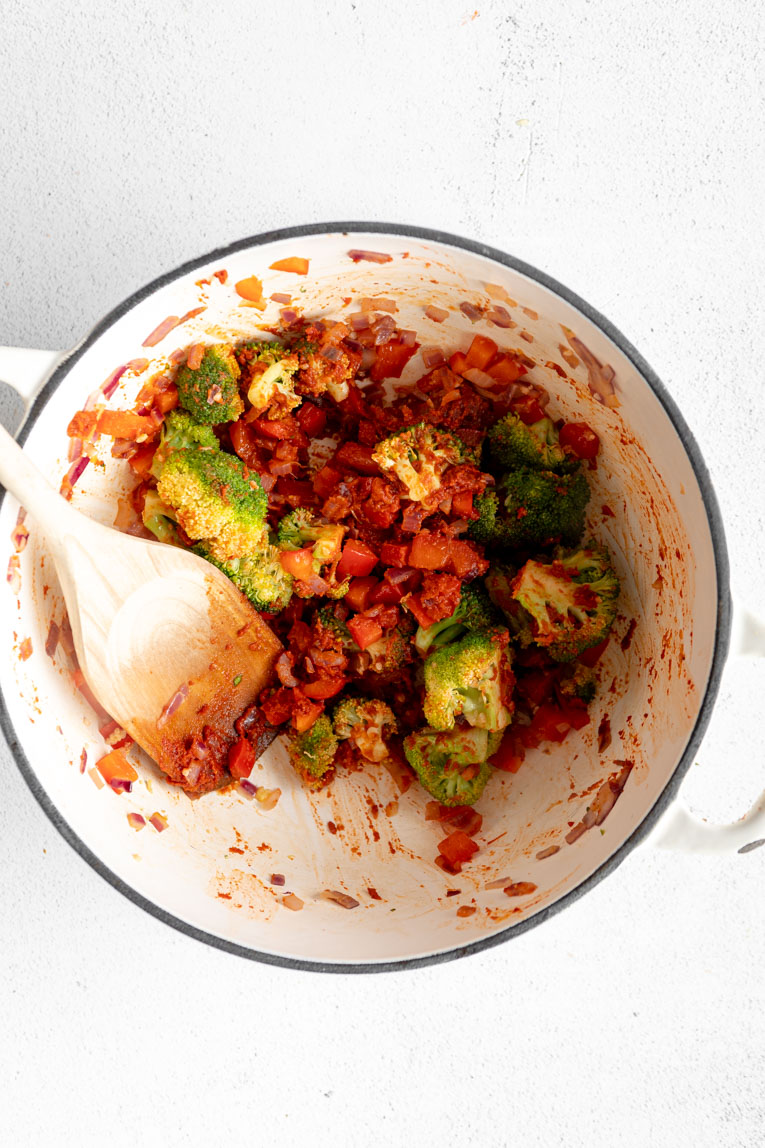 Veggies being cooked in red curry paste.
