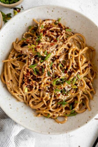 Sesame Tahini Noodles in a white bowl with chives, sesame seeds, and red pepper flakes.