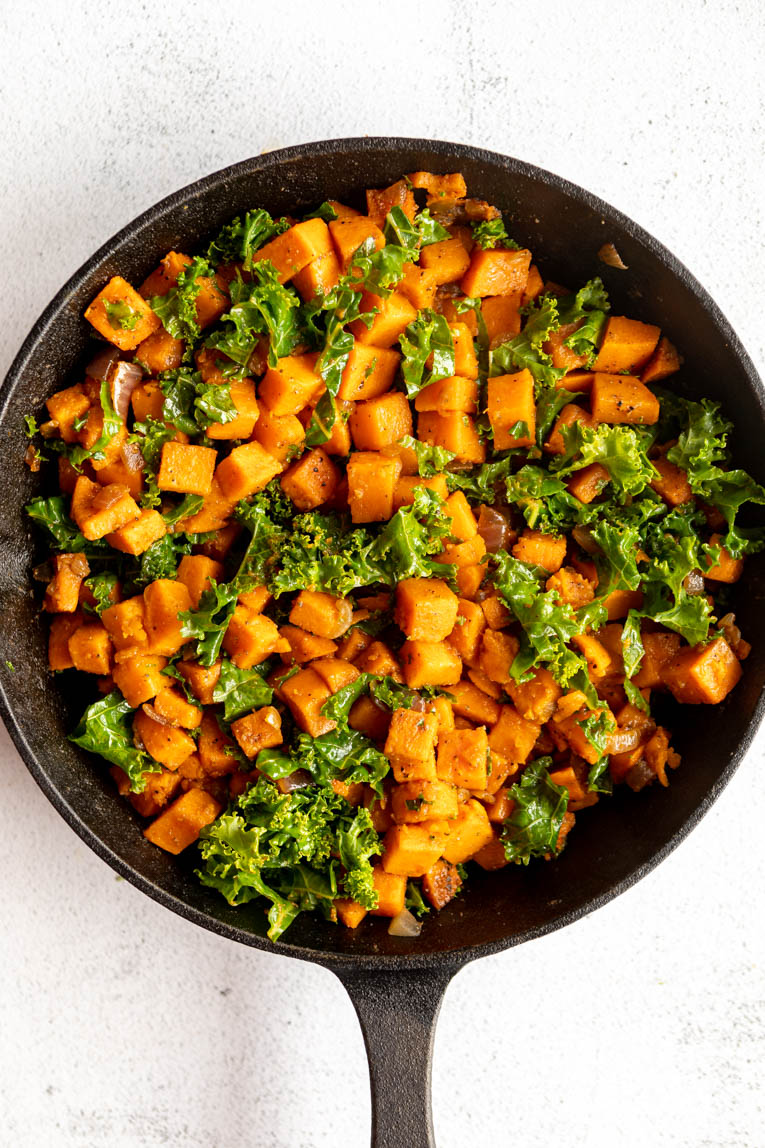 Sweet potatoes and kale being cooked in a skillet.