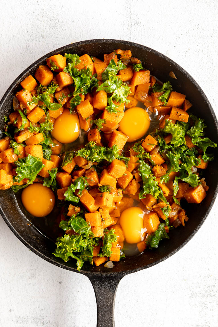 Eggs cooked in a skillet with sweet potatoes and kale.