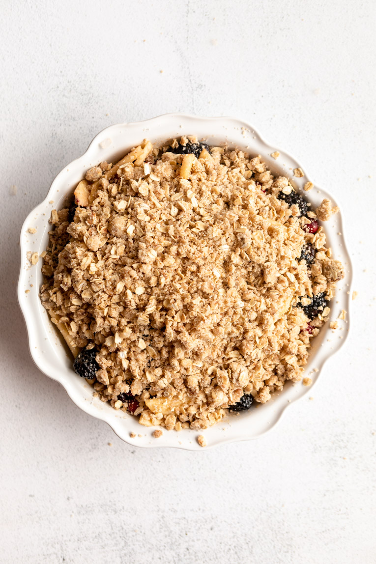 Apple blackberry cranberry crumble in a pie dish before baking.