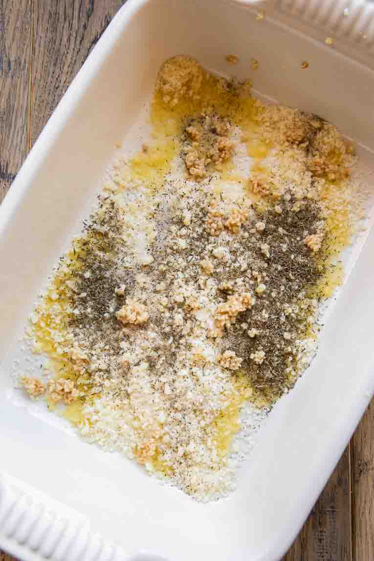 Olive oil, seasoning, and parmesan in the bottom of a casserole dish.