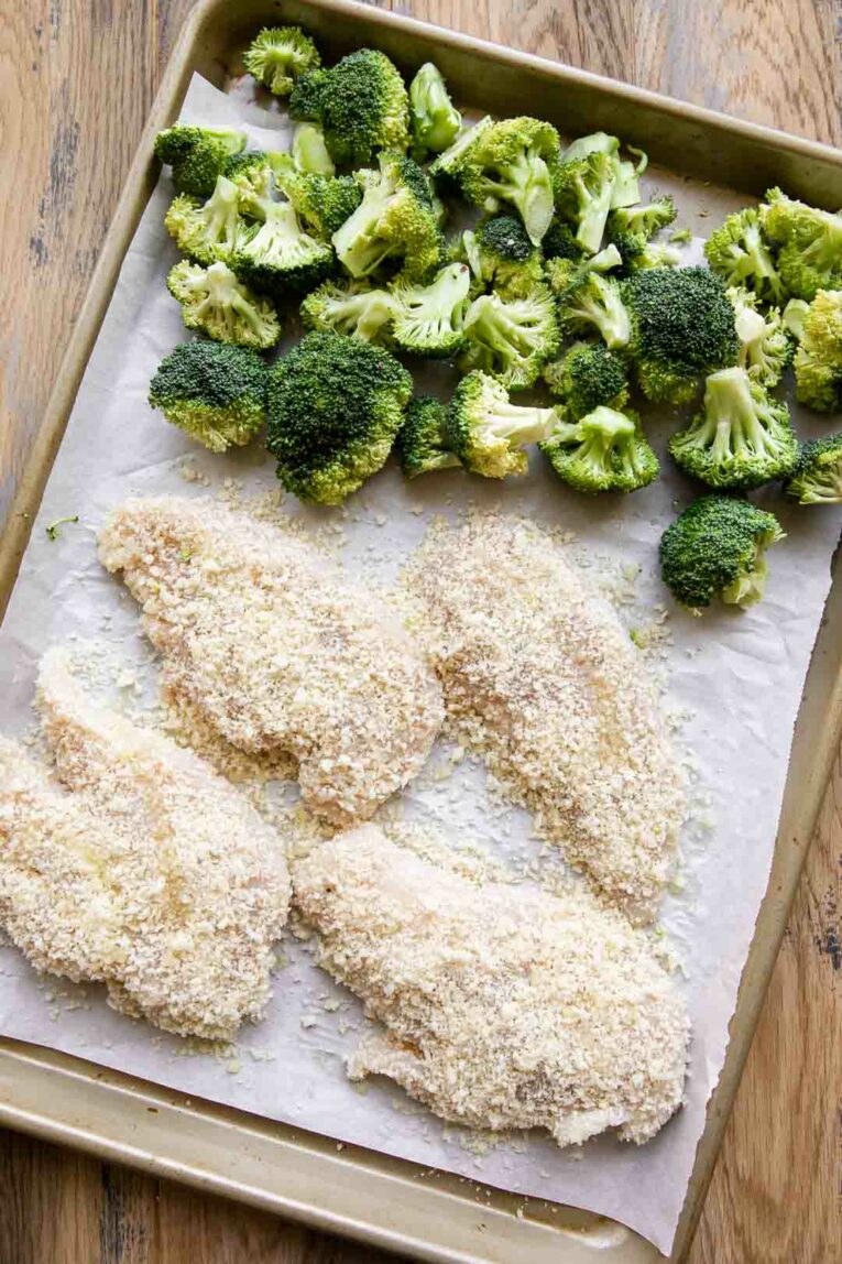 Chicken breasts coated in breadcrumbs on a sheet pan with broccoli.