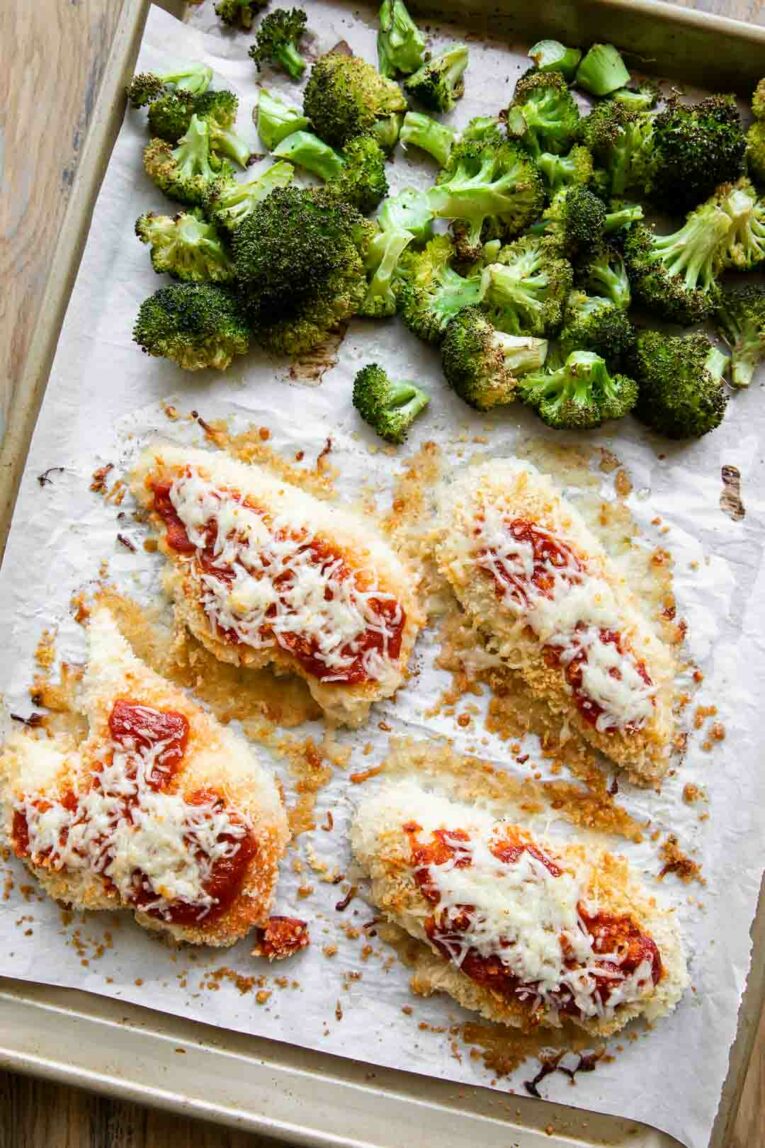 Marinara and mozzarella over breaded chicken baked with broccoli on a sheet pan.