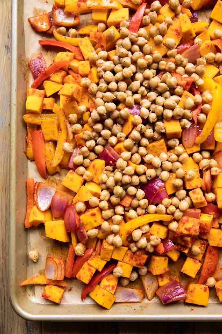 Seasoned chickpeas added to sheet pan with harissa veggies.
