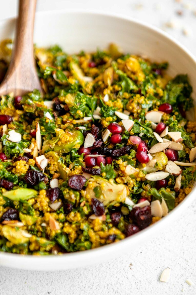 Roasted brussels sprouts, chopped kale, curry quinoa, cranberries, pomegranate arils, and almonds in a salad bowl.