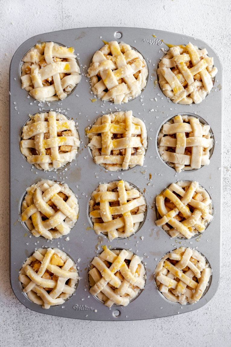 Mini apple pies in a muffin tin with lattice topping.