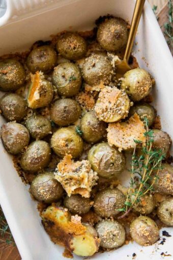 Close up of Crispy Garlic Parmesan Crusted Potatoes in a casserole dish with thyme.