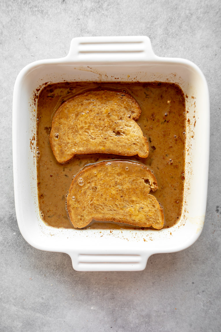 Brioche bread being dipped into an eggy french toast mixture.
