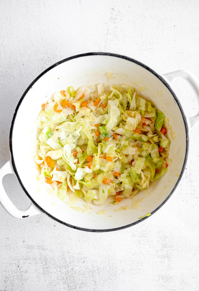 Cabbage and garlic added to onions and carrots in a dutch oven.
