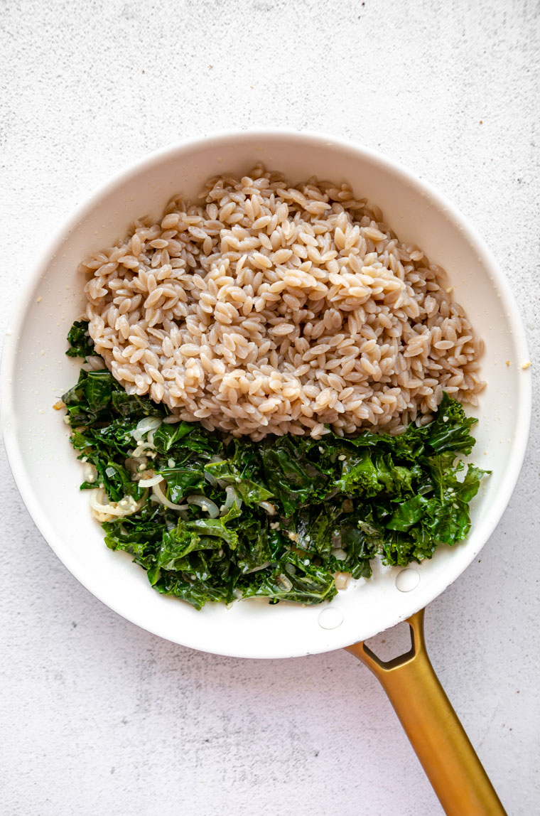 Cooked orzo and kale in a skillet with shallot and oil.