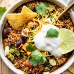 Easy Quinoa Chili recipe in a bowl with vegan sour cream, cilantro, lime, and chips.