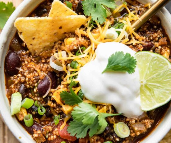Easy Quinoa Chili recipe in a bowl with vegan sour cream, cilantro, lime, and chips.