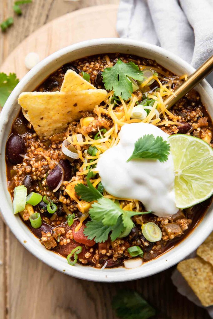 Easy Quinoa Chili recipe in a bowl with vegan sour cream, cilantro, lime, and chips.