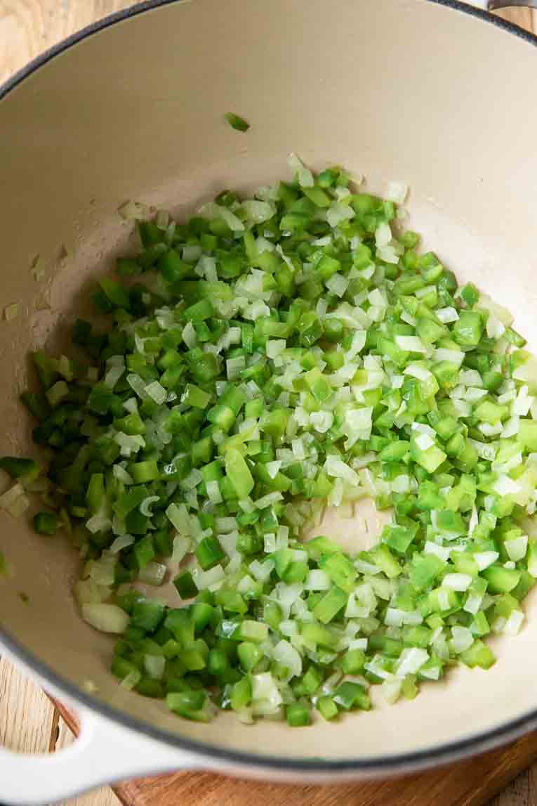 Diced onions and bell peppers being cooked in a dutch oven.
