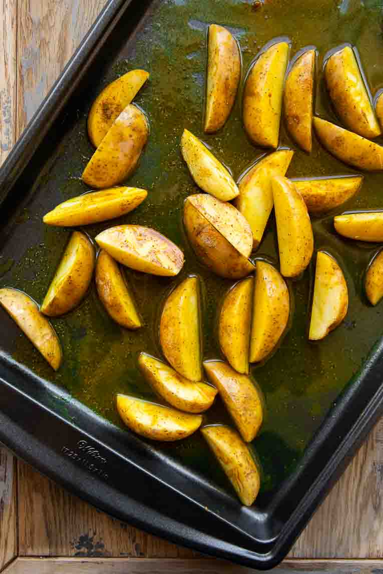 Turmeric potato wedges roasting on a pan.