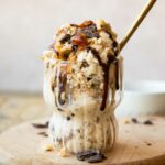 Ninja Creami Snickers Protein Ice Cream in a glass with toppings and a spoon.