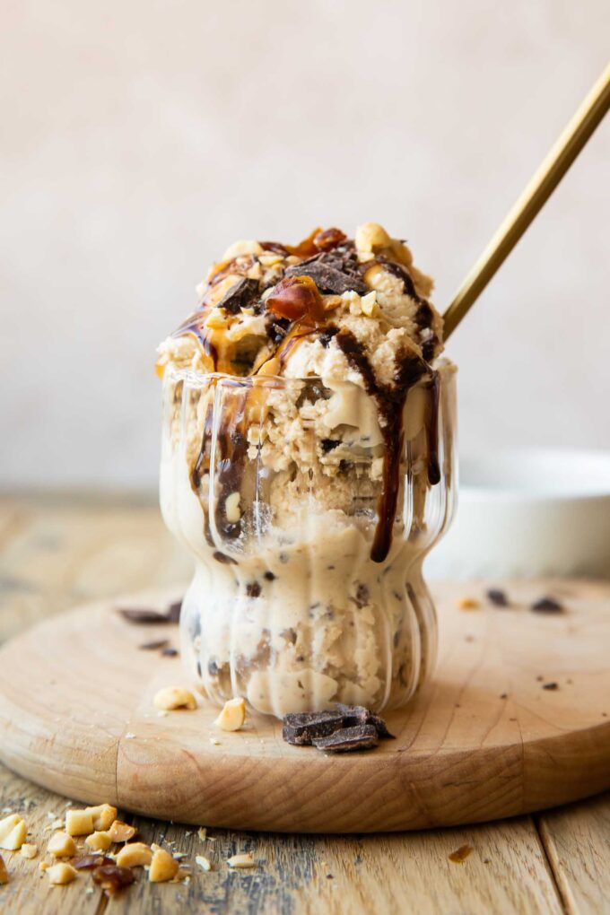 Ninja Creami Snickers Protein Ice Cream in a glass with toppings and a spoon.
