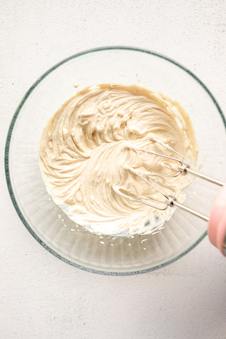 Cream cheese being mixed with an electric beater.