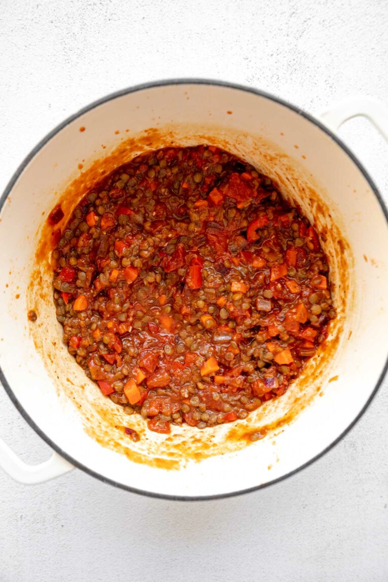 Onion, bell pepper, tomatoes, and carrots being sautéed in a dutch oven.