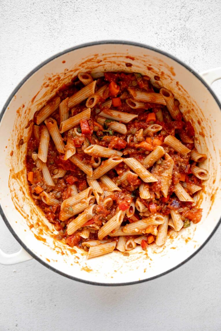 Pasta sauce and pasta being cooked in a dutch oven.