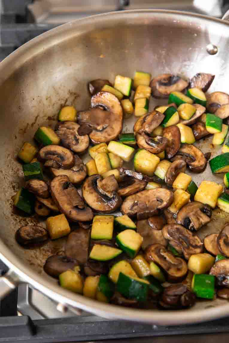 Mushrooms and zucchini being sautéed in a skillet.