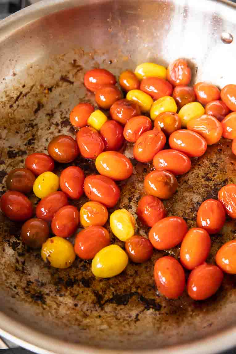 Blistered tomatoes cooking in a pan.